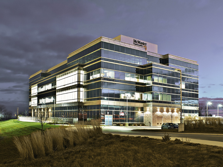Modern glass building with the McMaster University logo at the top of the building during the evening.